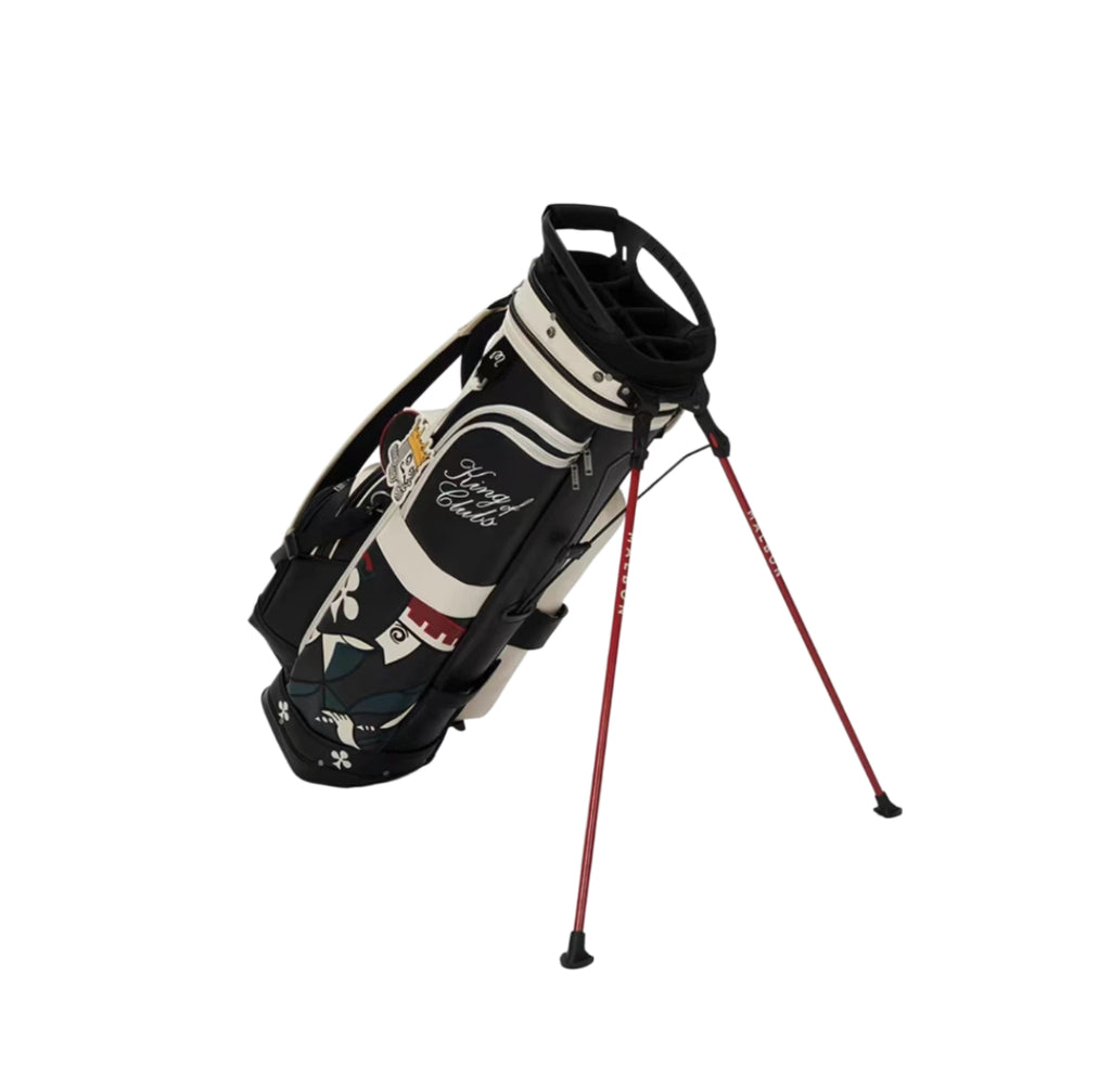 Angled shot of Malbon King of Clubs golf bag standing upright with deployed red dual-leg stand system, showcasing king-themed graphics and club organization top.