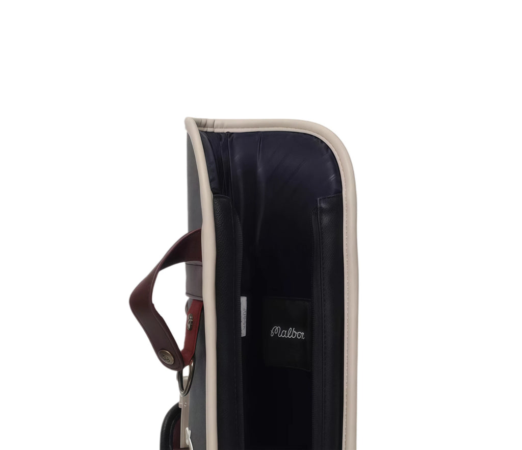 Interior view of Malbon Golf Sunday bag revealing navy blue padded lining, small brand tag with "Malbon" script, and structured design for golf club protection.