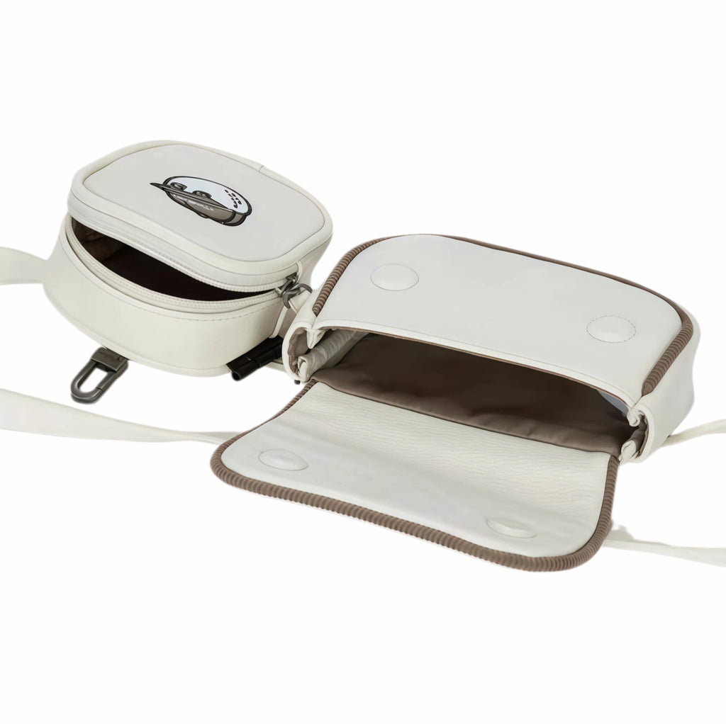 Front view of Malbon Golf dual pouch belt bag in cream white showing open compartments with brown interior lining, embroidered golf ball mascot, adjustable strap, and metal hardware
