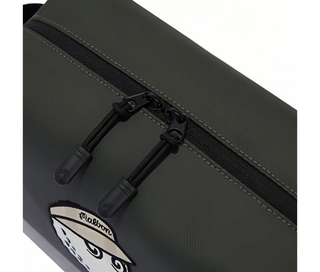 Close-up of Malbon Golf mini handbag top zipper featuring two black zip pulls with embossed "M" logo, smooth texture, and precise stitching along the seam