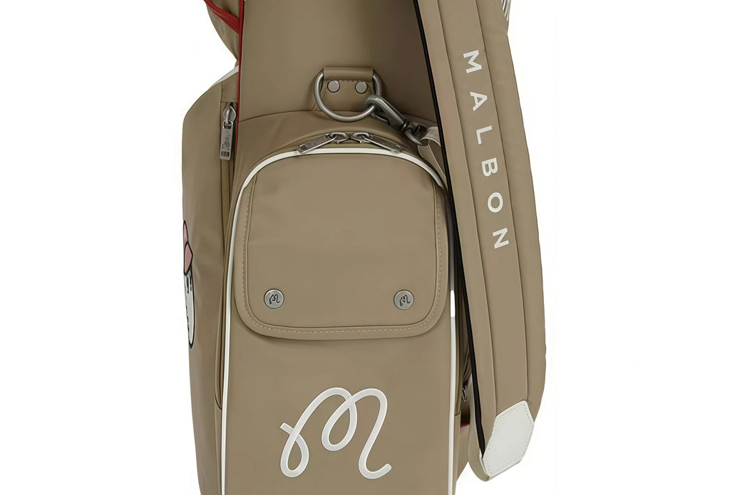 Close-up of Malbon Golf stand bag highlighting white "M" monogram logo, silver hardware, and padded shoulder strap with vertical "MALBON" text.