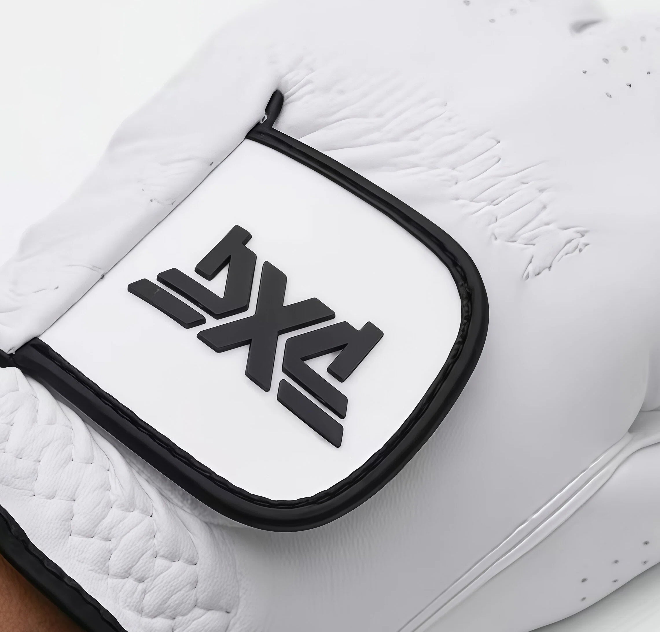  Close-up detail of the raised black PXG logo on the white synthetic leather of the Tour golf glove, highlighting the premium craftsmanship and texture.