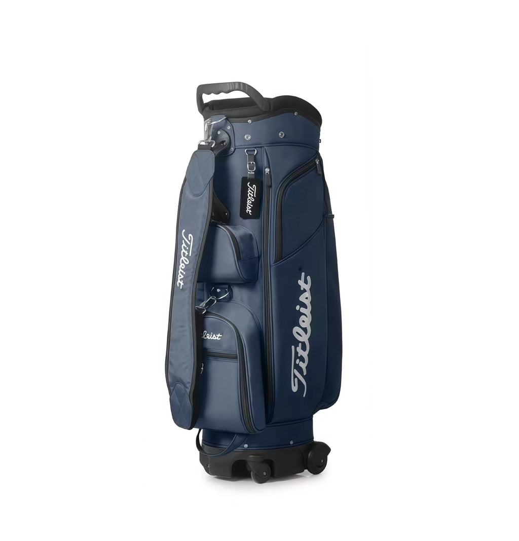 Side view of the Titleist Travel Trolley Bag in navy blue, featuring a padded shoulder strap, dual wheels, and multiple zippered compartments. Includes "Titleist" script logo and retractable top handle for easy transport.

